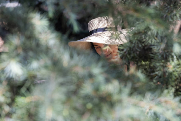 Beautiful young woman with a straw hat hidden from the camera, in the park. - Photo, Image
