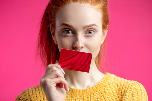 Happy beautiful ginger woman holding credit card isolated on pink background. - Foto, imagen