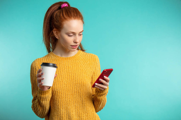 Young redhaired woman with coffee and smartphone isolated over b - Фото, зображення