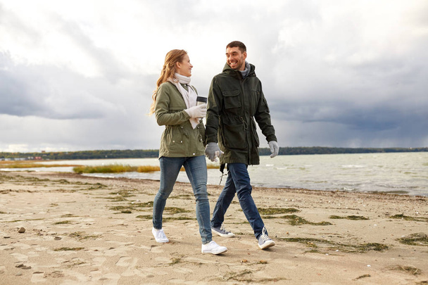 couple with tumbler walking along autumn beach - Zdjęcie, obraz