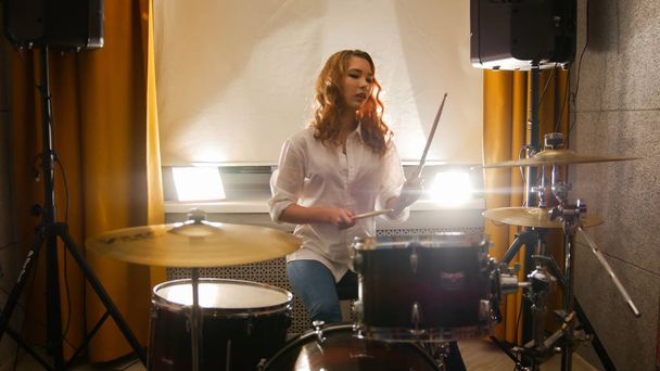 Redhead girl sits behind a drum set in the studio - Photo, Image