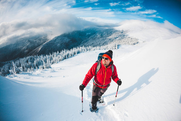 Egy férfi hótalp és trekking a hegyekben botok. Téli kirándulás. Hegymászás egy hegymászó, szemben a gyönyörű eget felhők. Aktív életmód. Megmásztuk a hegyet, a hóban. - Fotó, kép
