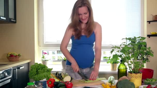 Těhotná žena krájení celer s nožem na salát na prkénku - Záběry, video