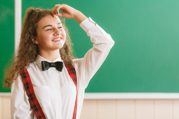 schöne junge Schülerin in Schuluniform, die auf dem Hintergrund der Schultafel steht - Foto, Bild