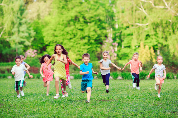 Многие дети, мальчики и девочки бегают в парке в солнечный летний день в повседневной одежде
 - Фото, изображение