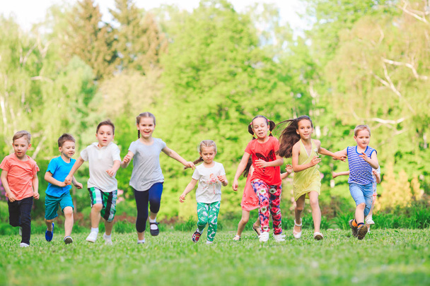 Muitas crianças, meninos e meninas diferentes correndo no parque no dia ensolarado de verão em roupas casuais
 - Foto, Imagem