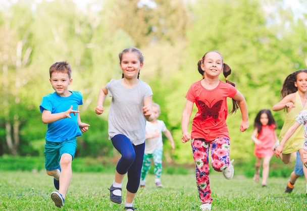 Muitas crianças, meninos e meninas diferentes correndo no parque no dia ensolarado de verão em roupas casuais
 - Foto, Imagem