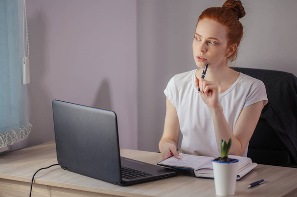 Portrait of redhaired young woman with laptop sitting at the tab - Foto, afbeelding