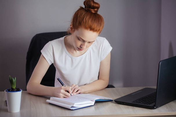 Portret van roodharige jonge vrouw met laptop zitten aan de tafel - Foto, afbeelding