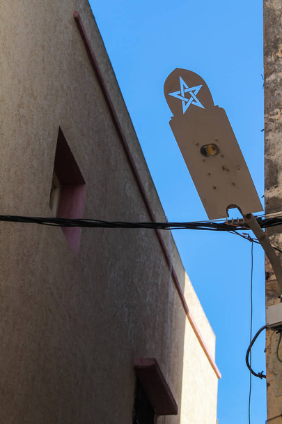 Ongebruikelijke ontwerp van een straat lamp, gemaakt van staal, met een teken van Marokko. Gebouw op de achtergrond. Blauwe hemel. Rabat, Marokko. - Foto, afbeelding