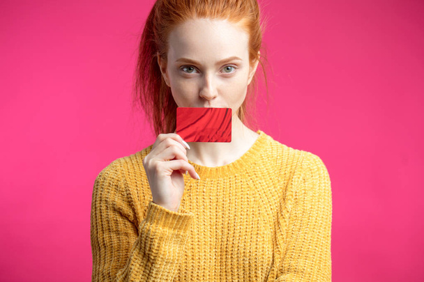 Happy beautiful ginger woman holding credit card isolated on pink background. - 写真・画像