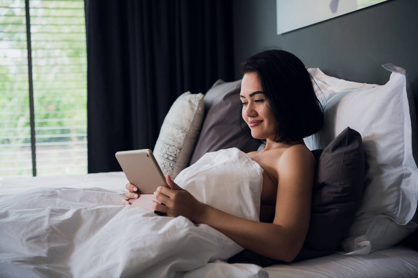 Γυναίκα χαλαρώνοντας στο κρεβάτι χρησιμοποιώντας ψηφιακό Tablet για κλήση βίντεο - Φωτογραφία, εικόνα