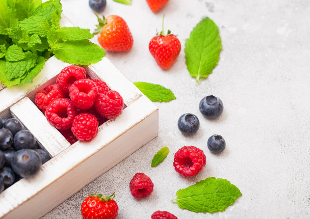 Fresh raw organic berries isolated in white wooden box on kitchen table background. Close up. Strawberry, Raspberry, Blueberry and Mint leaf - Фото, зображення