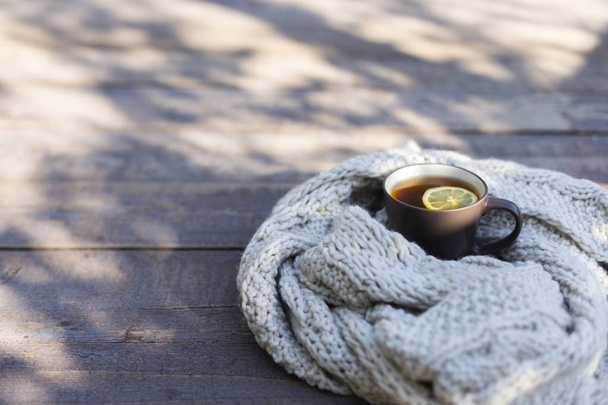 Cup of tea with lemon, knitted scarf near at wood background outdoor - Фото, зображення