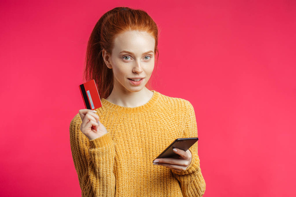 Portrait of cute ginger girl using smartphone isolated on pink background - Foto, afbeelding