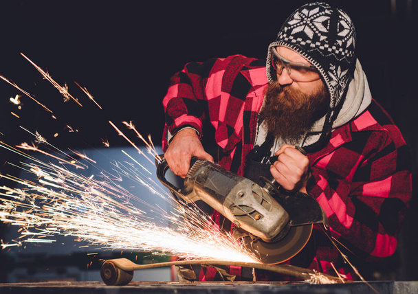 Worker Using Angle Grinder in Factory and throwing sparks. The employee of the service station produces body repair with a welding machine in hand sparks - Фото, зображення