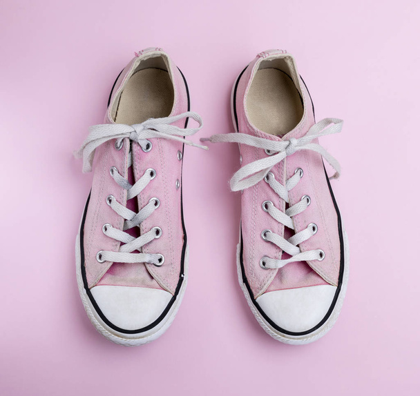 pair of old worn pink sneakers with white laces on a pink background, top view - Photo, Image