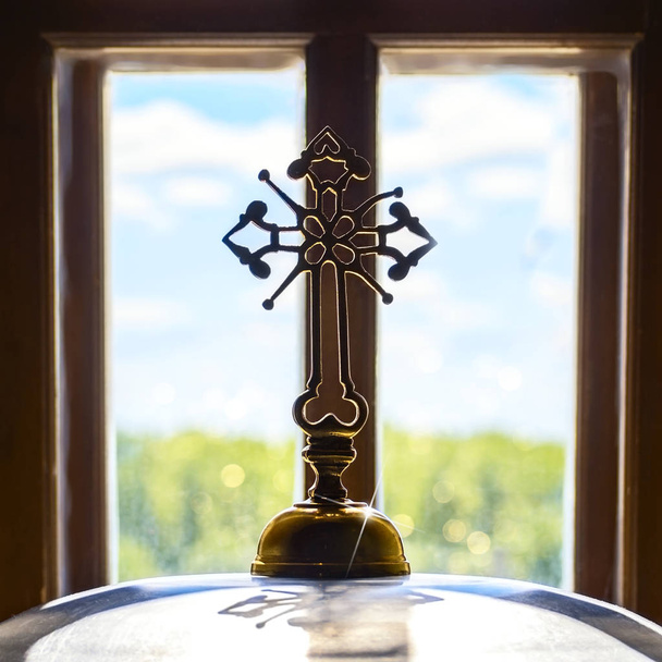 Церковный ортодоксальный крест напротив окна пейзаж солнца лучи синего неба зеленой травы. Концепция православного религиозного просвещения для защиты мирной жизни духовенства
 - Фото, изображение