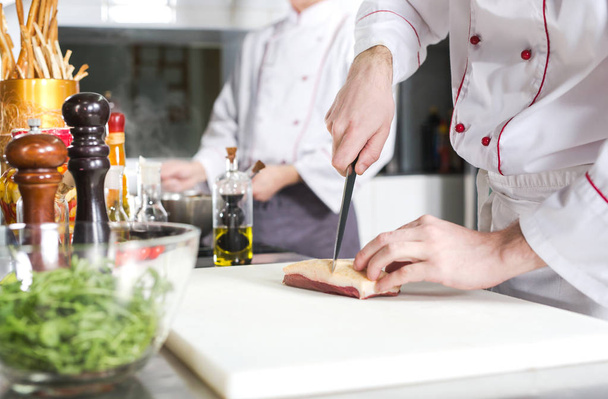 Chef cutting meat on chopping board, professional cook holding knife and cutting meat in restaurant - Photo, Image