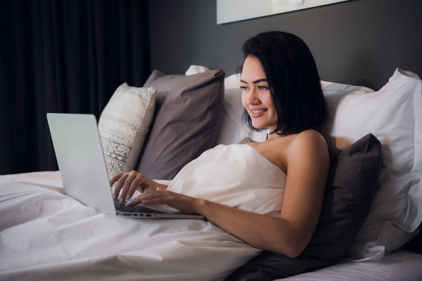 Kobieta pracuje na komputerze laptop leżąc na łóżku w domu. - Zdjęcie, obraz