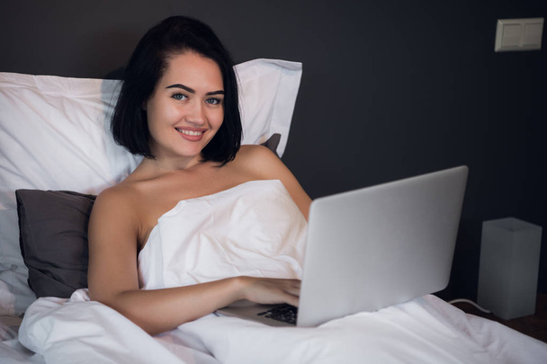 Güzel bir kadın yatakta yatan ve telefon görüşmesi. Onu laptop evde kullanan genç kız. Güzel kadın evde rahatlatıcı. - Fotoğraf, Görsel