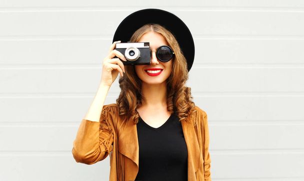 Fashion woman with retro film camera in black round hat, brown jacket on gray wall background - Foto, afbeelding