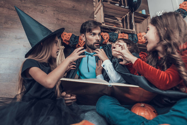 Man and Children in Halloween Costumes having Fun. Cute Smiling Kids and Adult Man wearing Scary Halloween Costumes Sitting on Floor next to Carved Pumpkins. Celebration of Halloween - Foto, Imagem