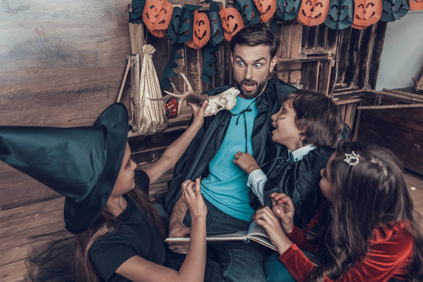 Man and Children in Halloween Costumes having Fun. Cute Smiling Kids and Adult Man wearing Scary Halloween Costumes Sitting on Floor next to Carved Pumpkins. Celebration of Halloween - Fotografie, Obrázek
