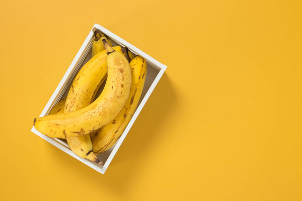 Boîte de bananes mûres sur fond jaune vif, avec espace de copie
. - Photo, image