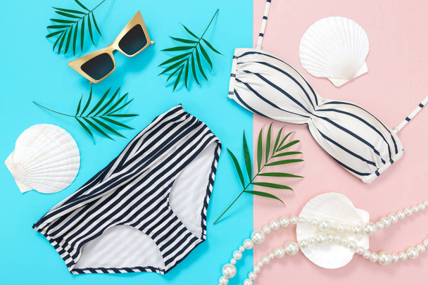 Vacaciones de verano plana yacía sobre fondo azul y rosa. Bikini, gafas de sol, hojas de palma, collar de perlas y conchas marinas
. - Foto, Imagen