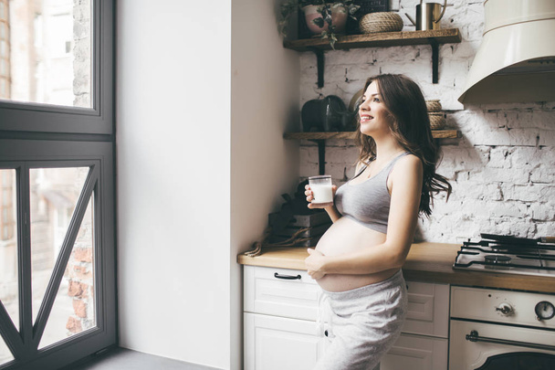 Pretty pregnant woman in kitchen with cup of milk - 写真・画像