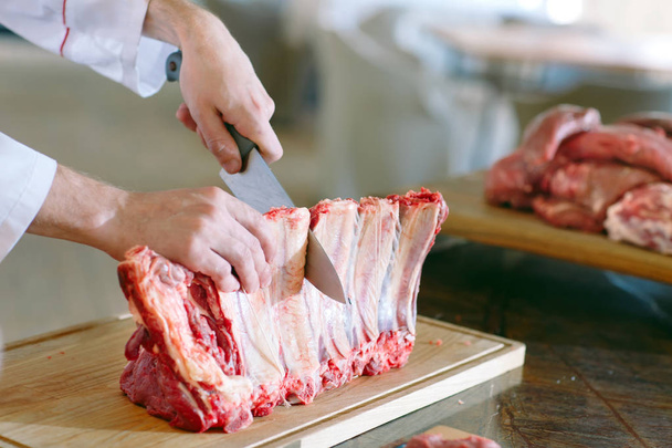 hands of male cook cutting raw ribs with a knife in a restaurant - Foto, imagen