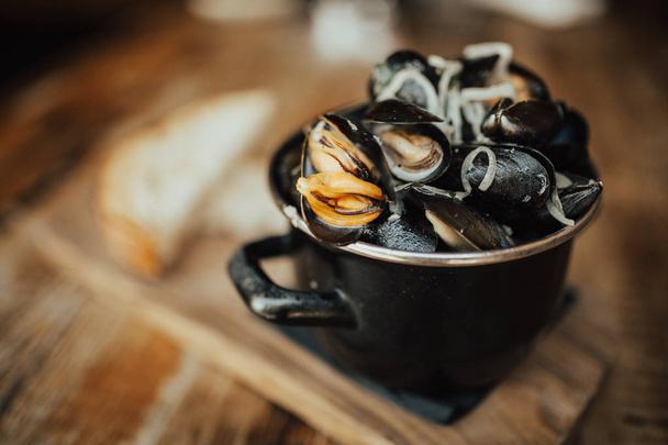 Mussels in a black copper bowl served on the wooden board. Close up indoor shot, food and restaurant concept. - Fotoğraf, Görsel
