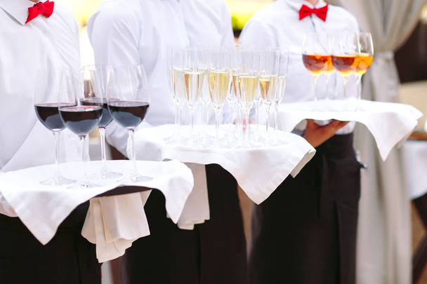 waiters greeting guests with alcoholic drinks. Champagne, red wine, white wine on trays. - Photo, Image