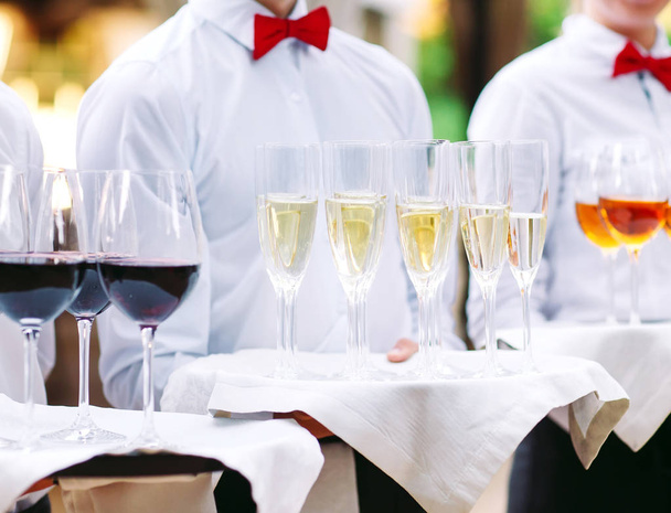 camareros saludan a los huéspedes con bebidas alcohólicas. Champán, vino tinto, vino blanco en bandejas
. - Foto, imagen