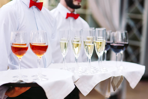 Die Kellner begrüßen die Gäste mit alkoholischen Getränken. Champagner, Rotwein, Weißwein auf Tabletts. - Foto, Bild