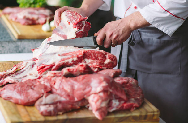 male cook cutting raw meat with knife in a restaurant - Zdjęcie, obraz