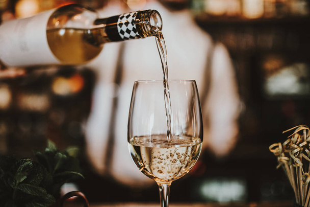 Close up shot of a bartender pouring white wine into a glass. Hospitality, beverage and wine concept.  - Fotó, kép