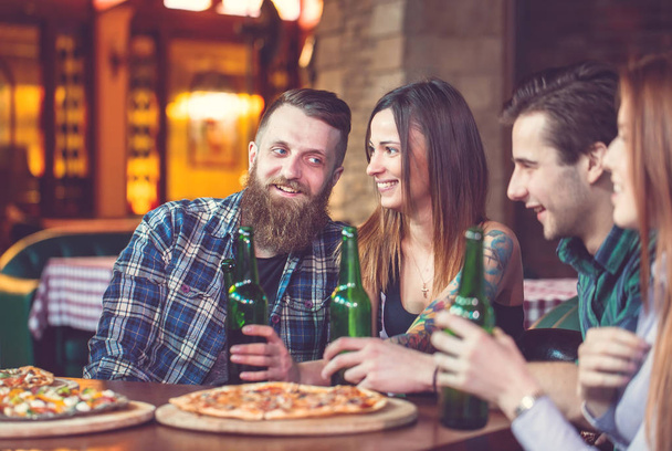Friends having a drinks in a bar, They are sitting at a wooden table with beers and pizza. - Foto, Imagem