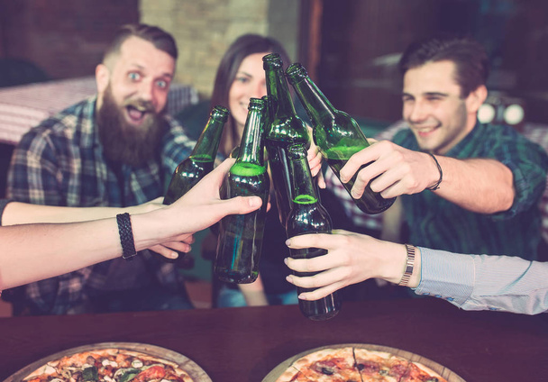Friends having a drinks in a bar, They are sitting at a wooden table with beers and pizza. - Fotoğraf, Görsel