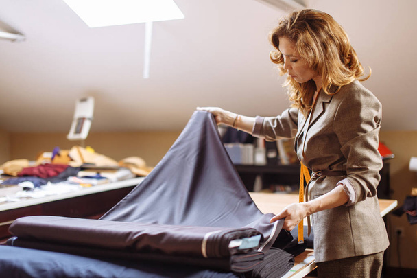 Designer de moda feminina trabalhando em tecido adequado com acessórios de costura na mesa
 - Foto, Imagem