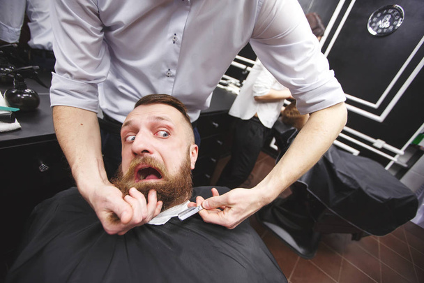 Bearded man with fear is sitting in a Barbershop. - Φωτογραφία, εικόνα