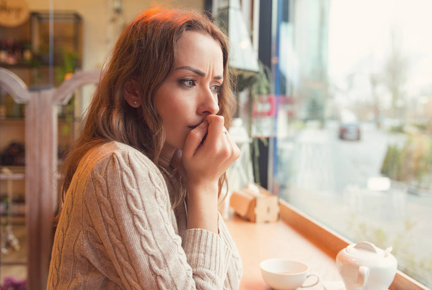 Nervous worried young woman biting nails and looking away sitting alone in a coffee shop - Foto, Imagem