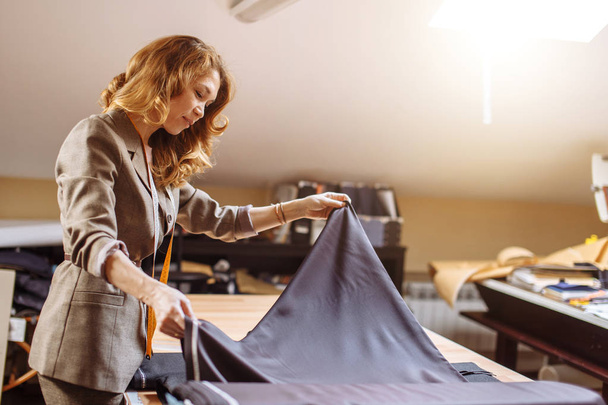 Female fashion designer working on suiting fabric with dressmaking accessories on table - Foto, imagen