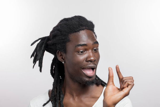 dark skinned man showing small thing while smiling and standing near white background - Foto, Imagen