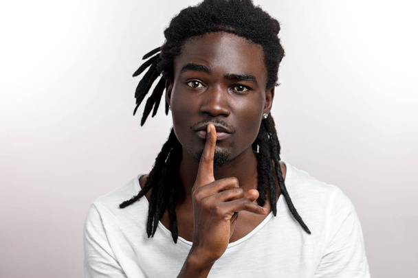dark-skinned young man gesturing as secret holding his index finger at his lips, saying Shh - Zdjęcie, obraz