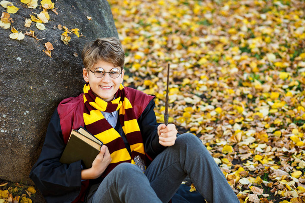 szemüveg fiú őszi parkban áll, pálca van a kezedben, könyv, visel a fekete öltöny és a csíkos sál. Mindenszentek napjának előestéje ruha, cosplay - Fotó, kép