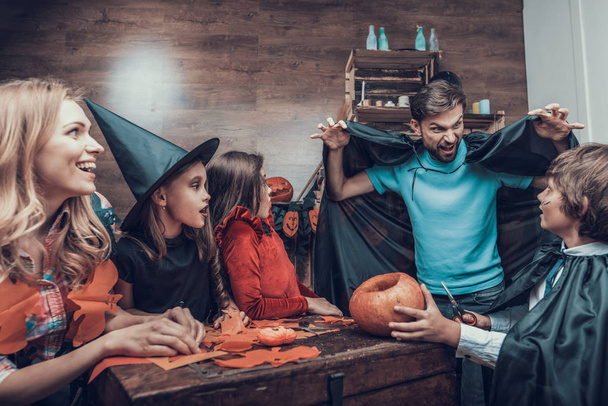 Family having Fun Making Halloween Decorations. Adorable Little Children and Young Parents in Costumes Sitting at Table and Cutting Colorful Pieces of Paper with Scissors. Celebration of Halloween - Photo, image