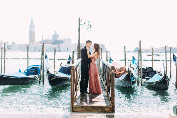 Couple posing on wooden pier near gondolas during honeymoon in Venice - Foto, Imagen