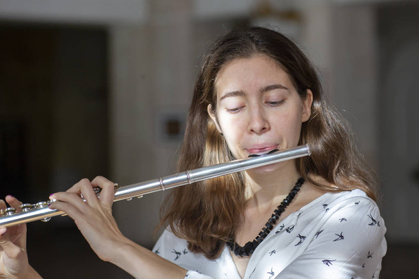 A beautiful woman posing while playing on a flute Genre portrait of young beautiful girlr Close-up - 写真・画像